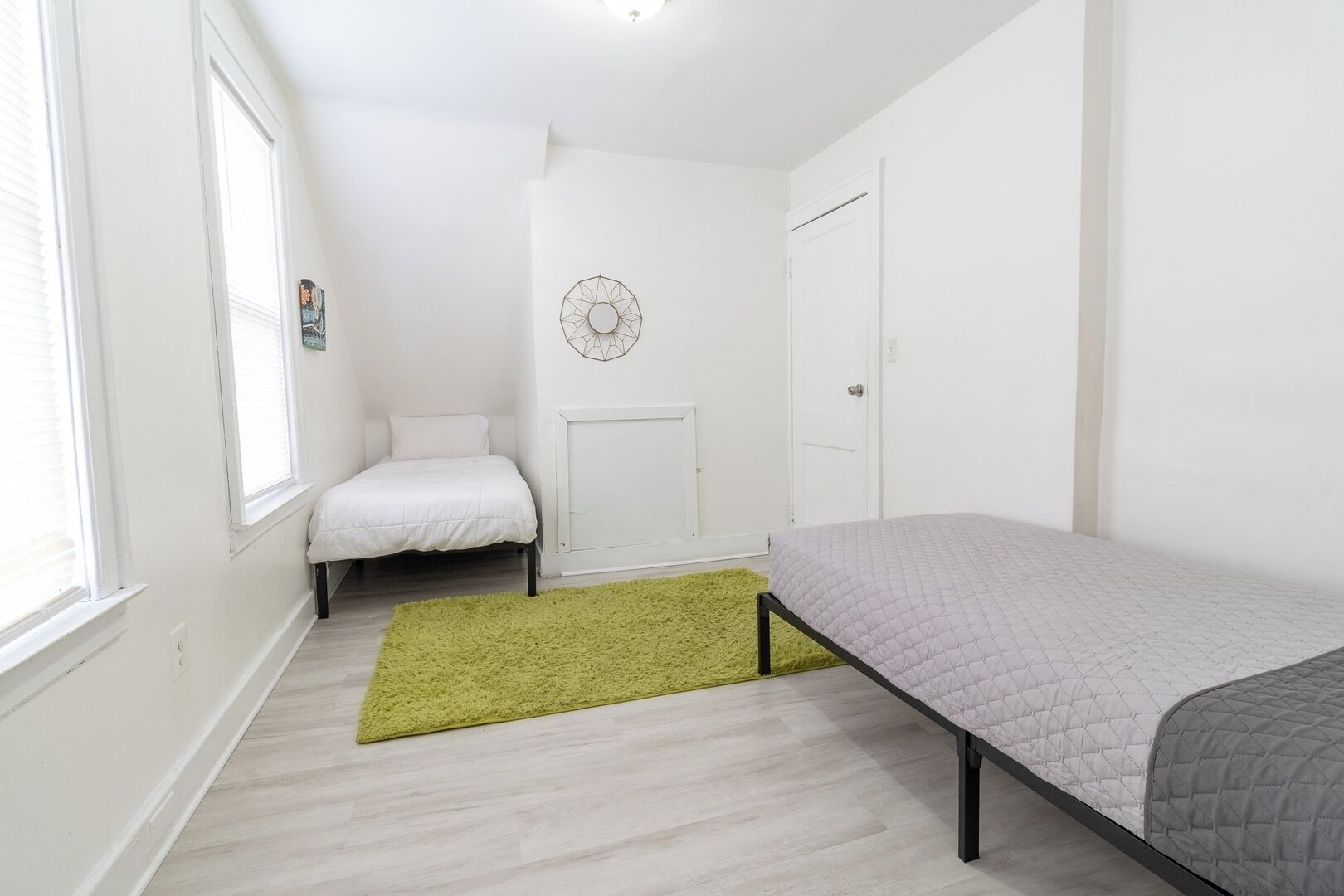 Une petite pièce lumineuse, avec deux lits, un tapis vert et un motif géométrique décorant le mur.