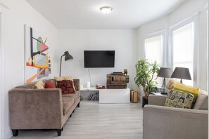 Una sala de estar moderna con un televisor de pantalla plana, dos sofás, una mesa de centro, una estantería y una planta en maceta.