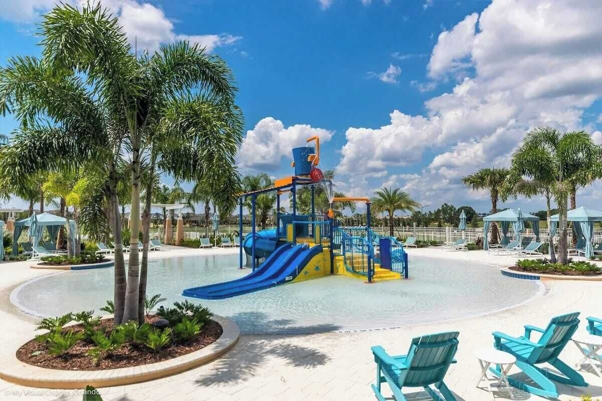 Ein Wasserpark mit einer blauen und gelben Spielkonstruktion, Palmen und Liegestühlen.