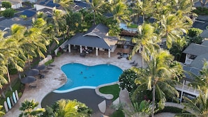 Vista aérea de un resort con piscina central, rodeado de palmeras y un pabellón cubierto.