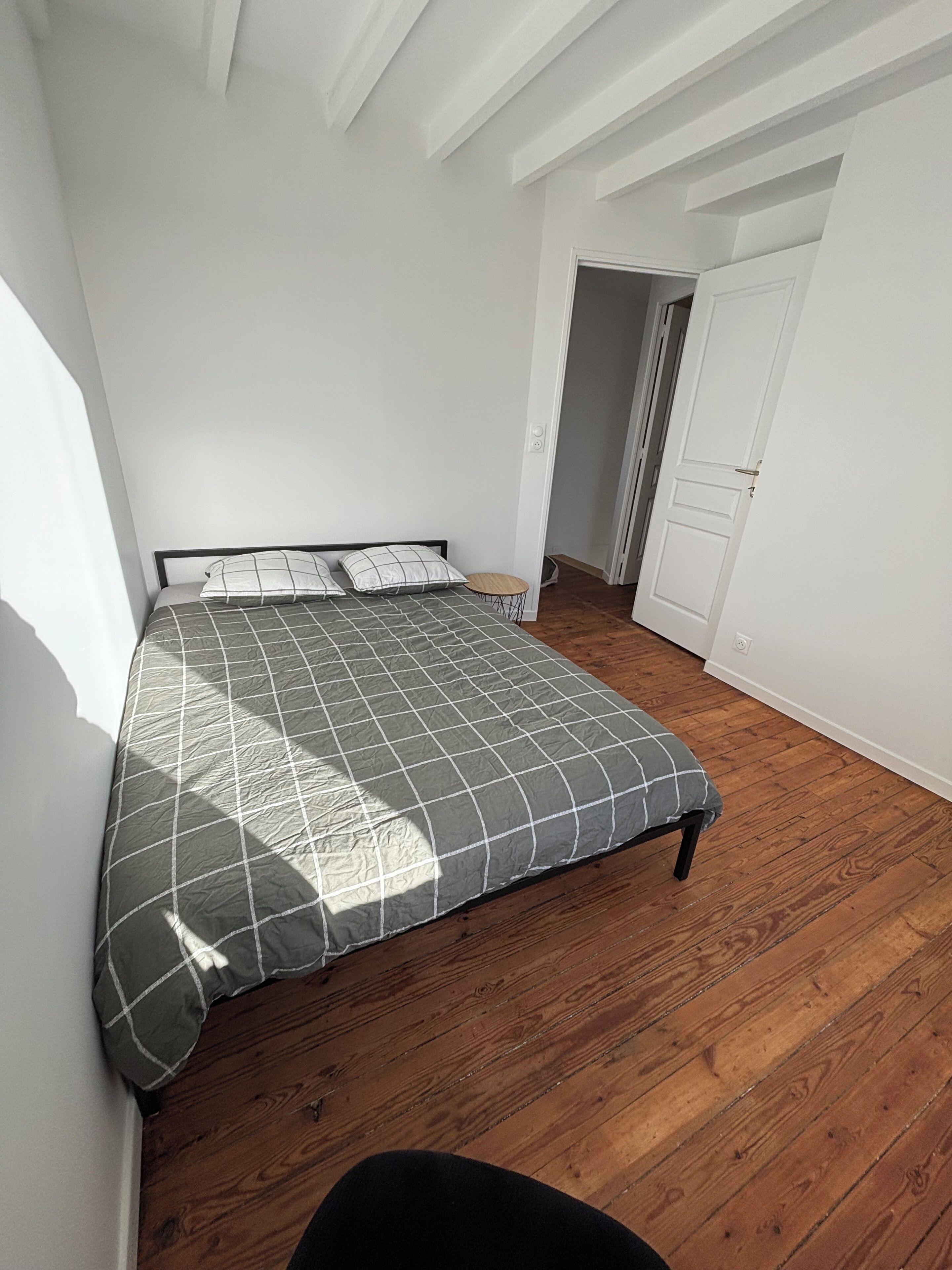 A bedroom with a bed, wooden flooring, white walls, and a door.
