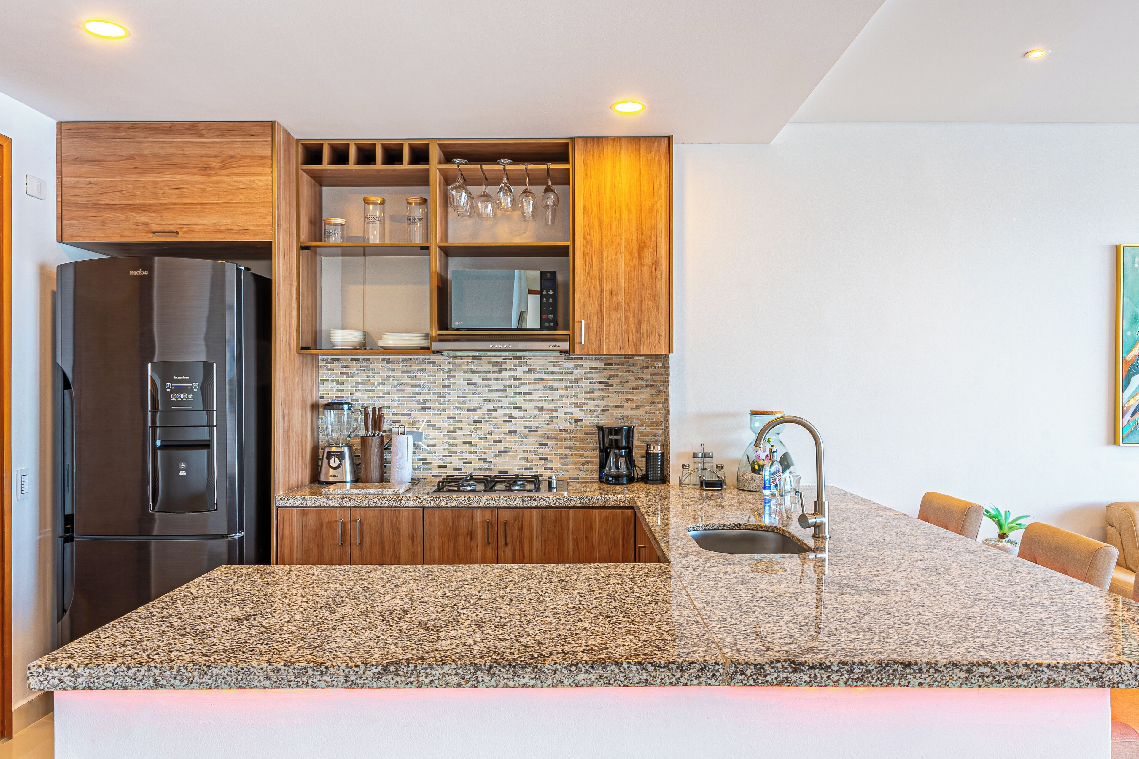 Una cocina moderna con encimera de granito, electrodomésticos de acero inoxidable, armarios de madera y un microondas integrado.