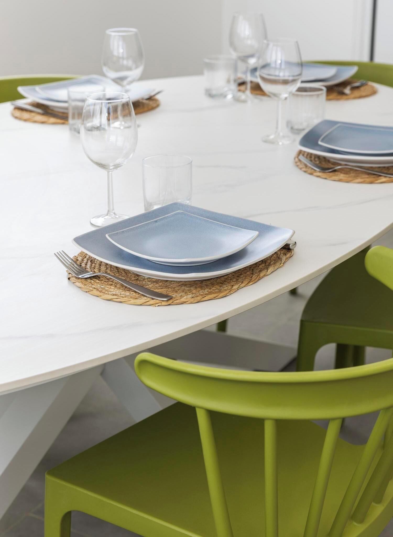 A dining table set with plates, cutlery, and glasses, surrounded by green chairs.
