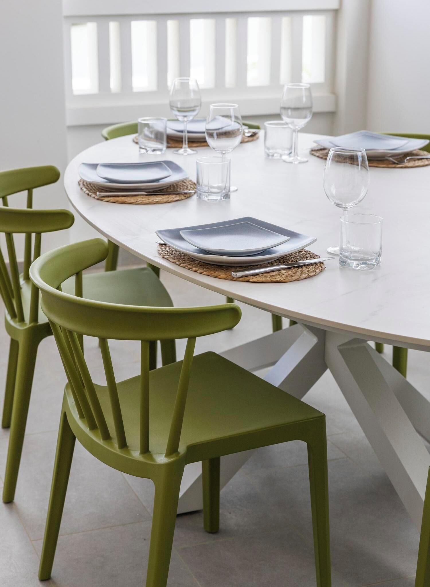 Une table de salle à manger ronde, avec des assiettes carrées et des verres transparents, entourée de chaises vertes.