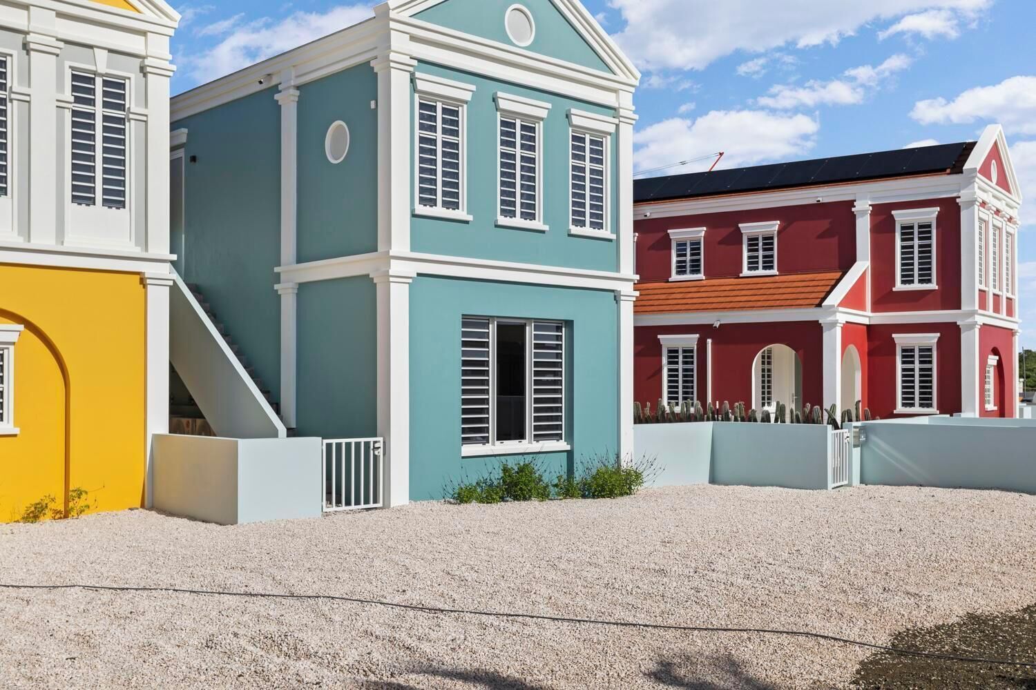 A row of colorful houses with distinct architectural styles, including a blue house with white shutters and a red house with a wooden roof.