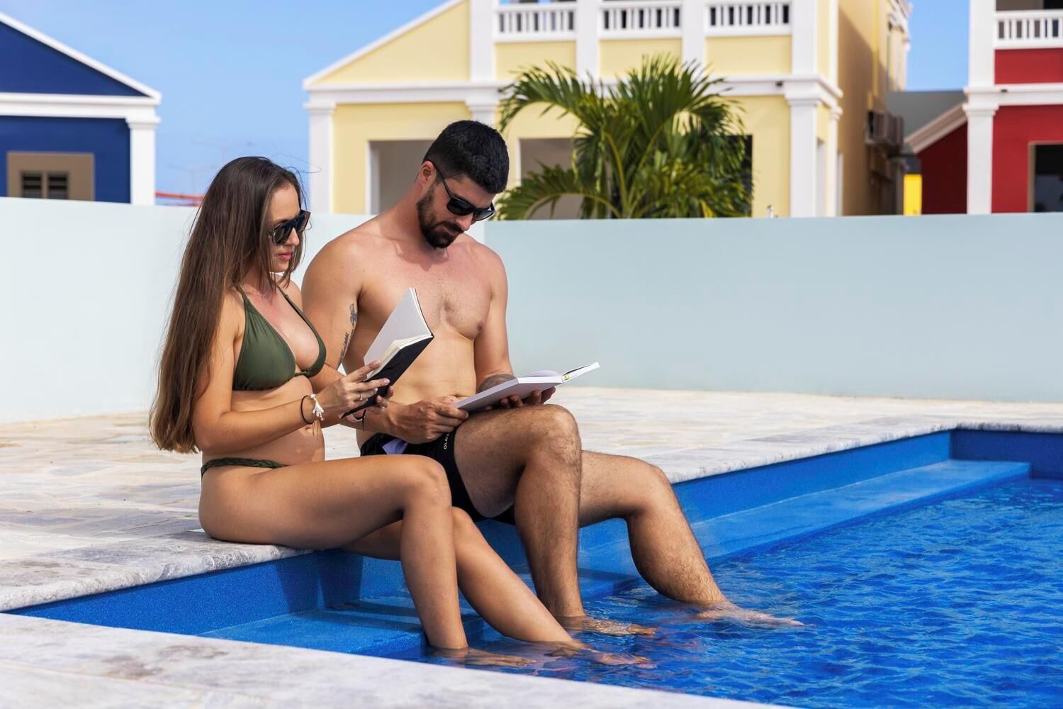 Two people sitting by a pool with a clear view of a building in the background.