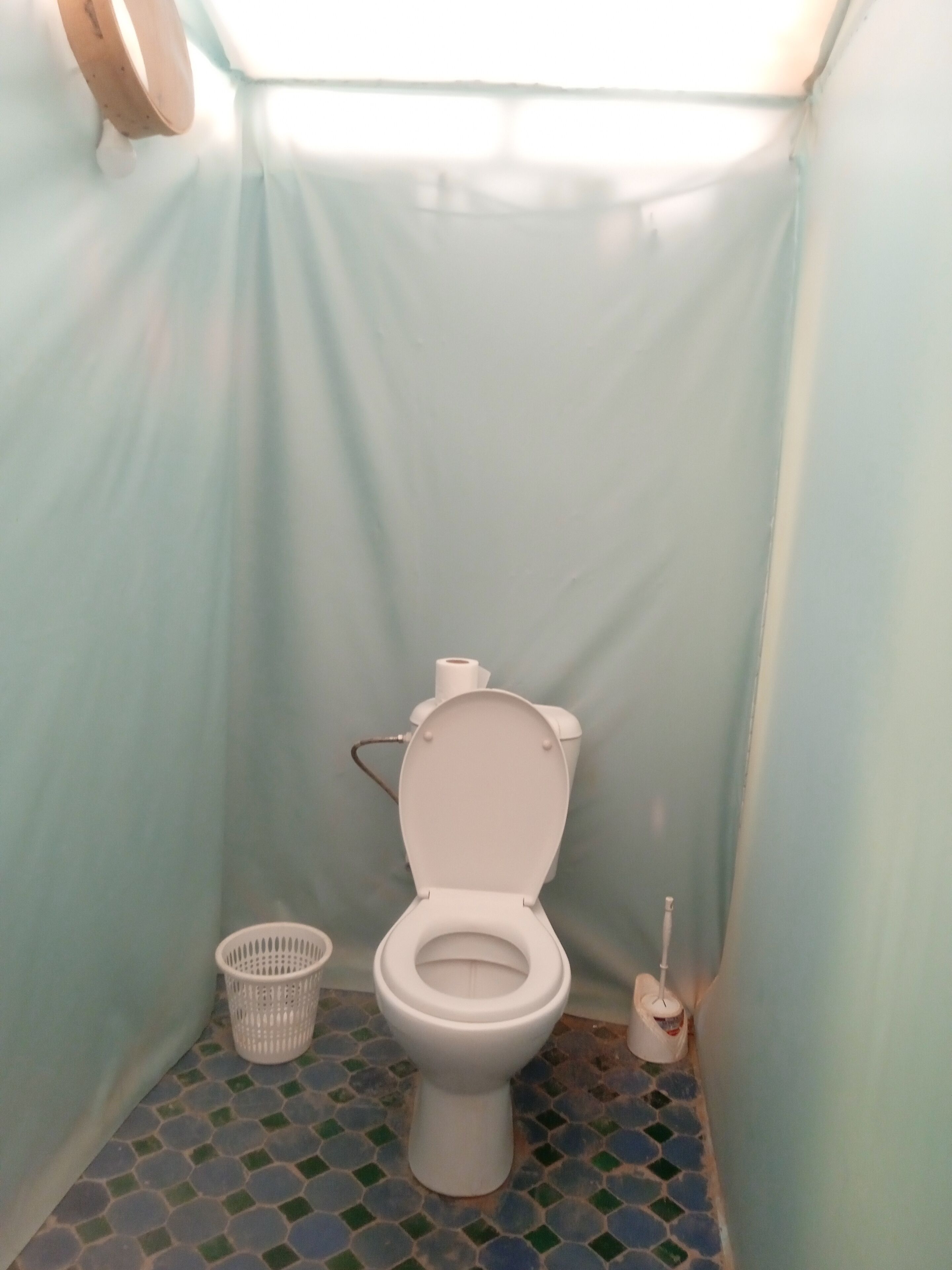 A small, enclosed bathroom with a toilet, a basket, and a toilet brush.