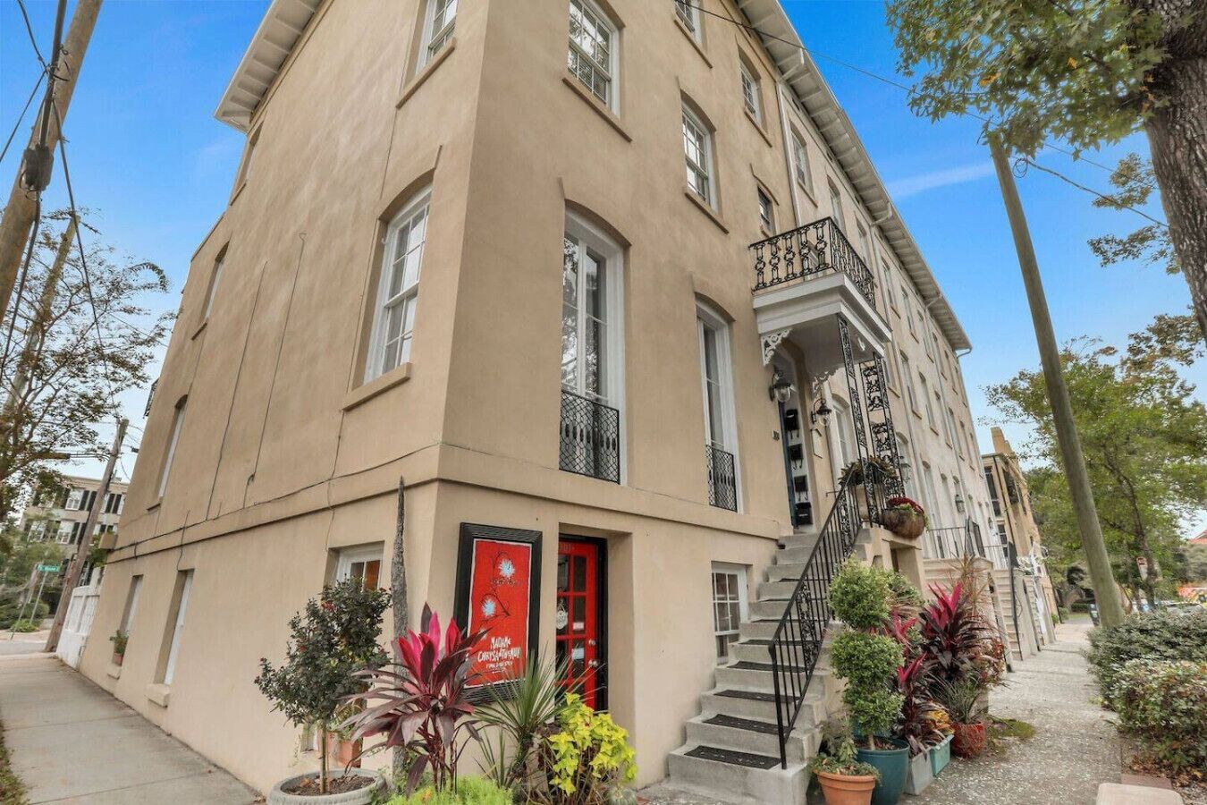 A beige building with a red door, multiple windows, and a staircase leading to a balcony.
