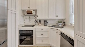 A compact kitchen with white cabinetry, a microwave, a coffee maker, and a dishwasher.