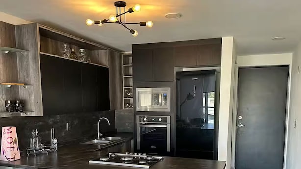 A modern kitchen with a central island, bar stools, stainless steel appliances, and a built-in microwave. - Luxury Apartment Fracc Element (San Agustín)