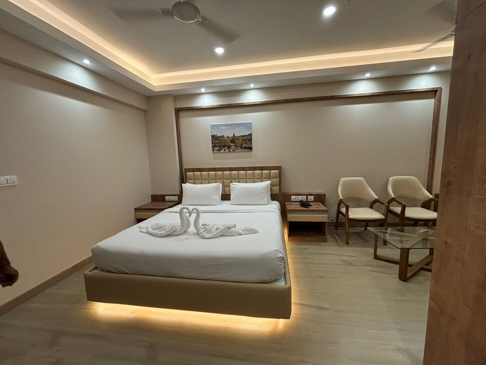 A modern hotel room with a large bed, a desk, two chairs, and a ceiling fan.
