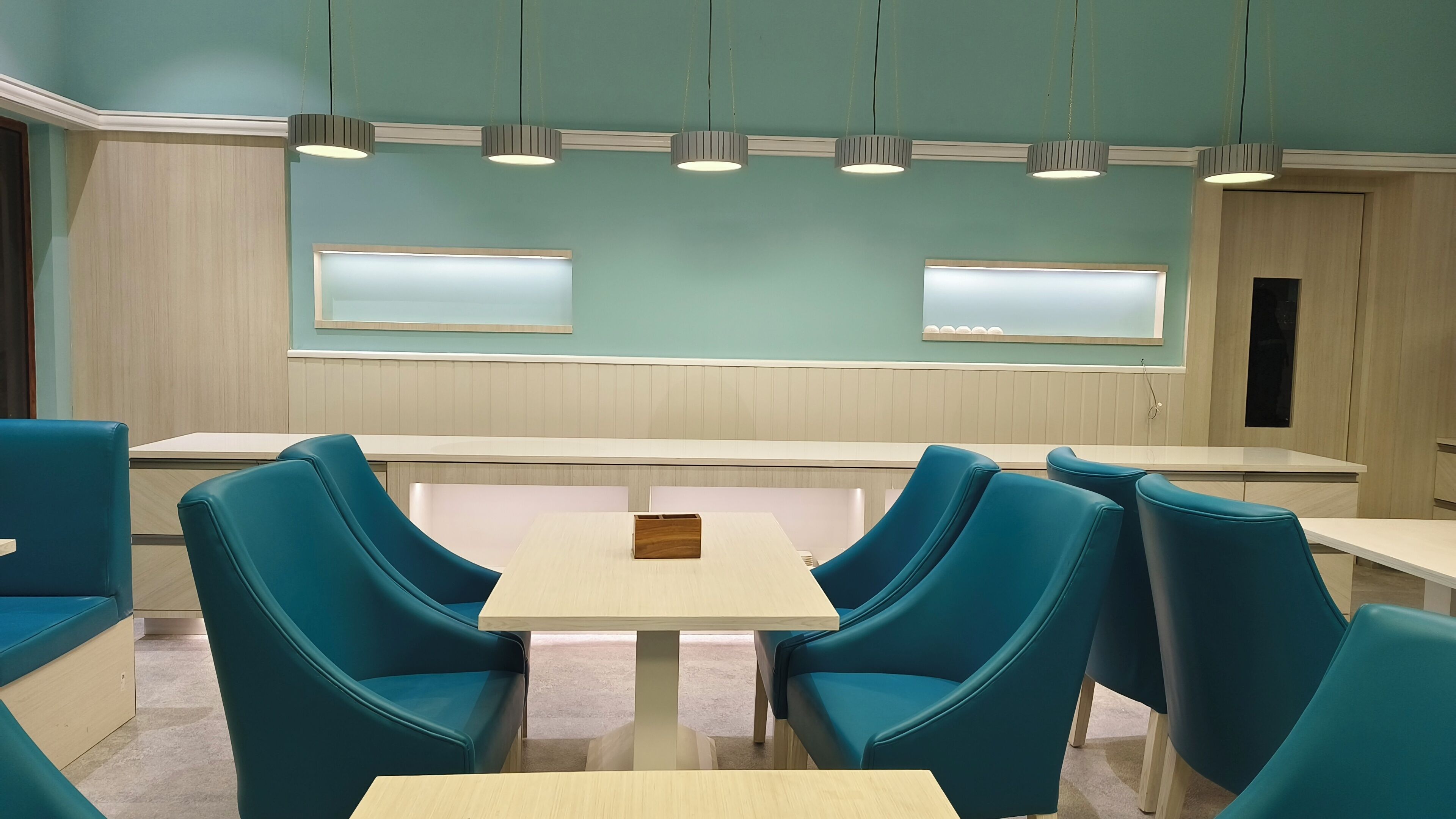 Un comedor moderno con sillas y mesas color turquesa, iluminación colgante y paneles de madera en las paredes.