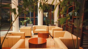 A modern lounge area with leather sofas and a wooden coffee table, surrounded by large windows and indoor plants. - The Pearl Club Resort (Bolpur)