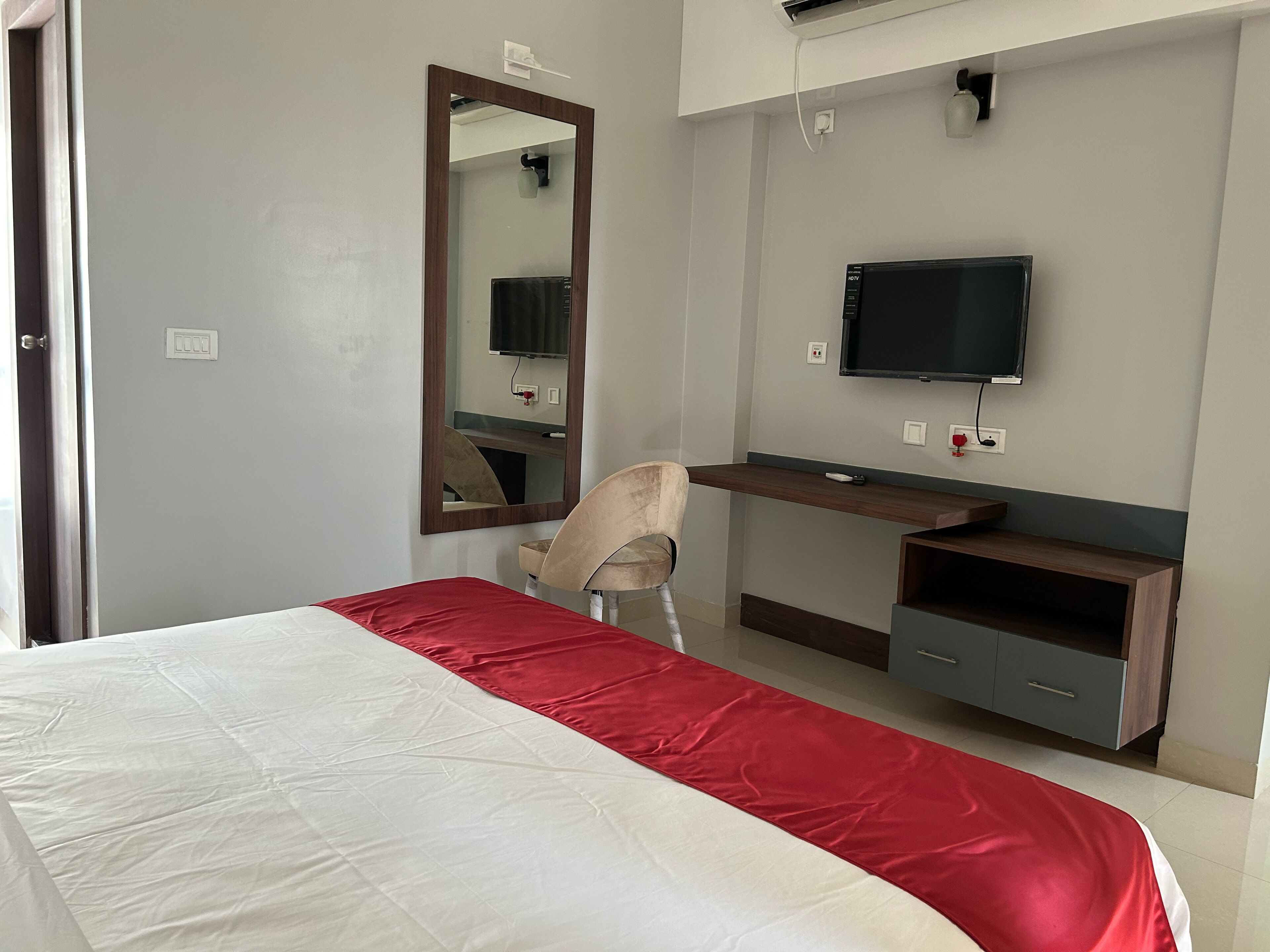 A hotel room with a bed, a desk, a chair, a TV, and a mirror.