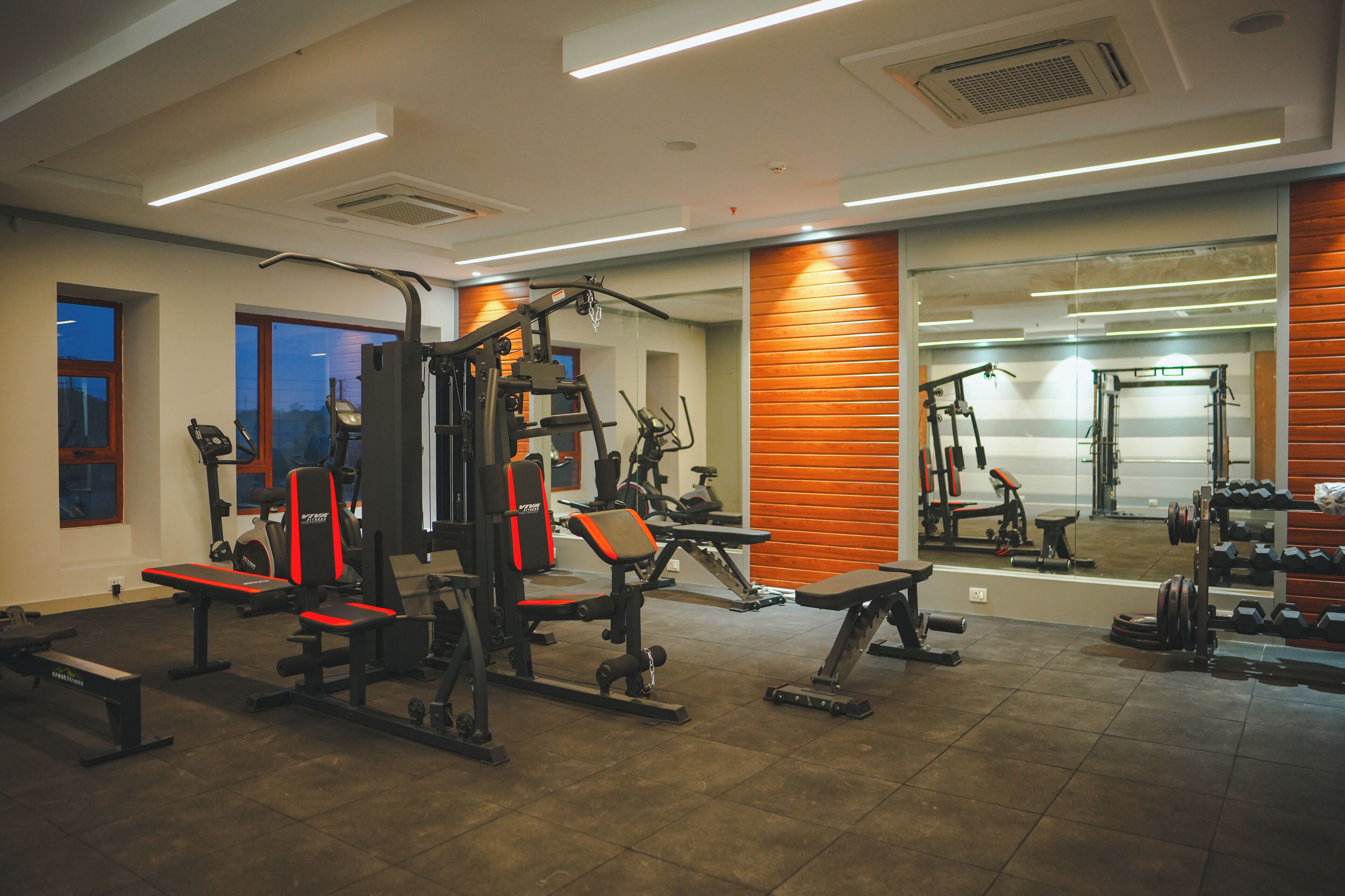 Een sportschool met diverse fitnessapparaten, grote ramen en een spiegel die de apparatuur weerspiegelt.