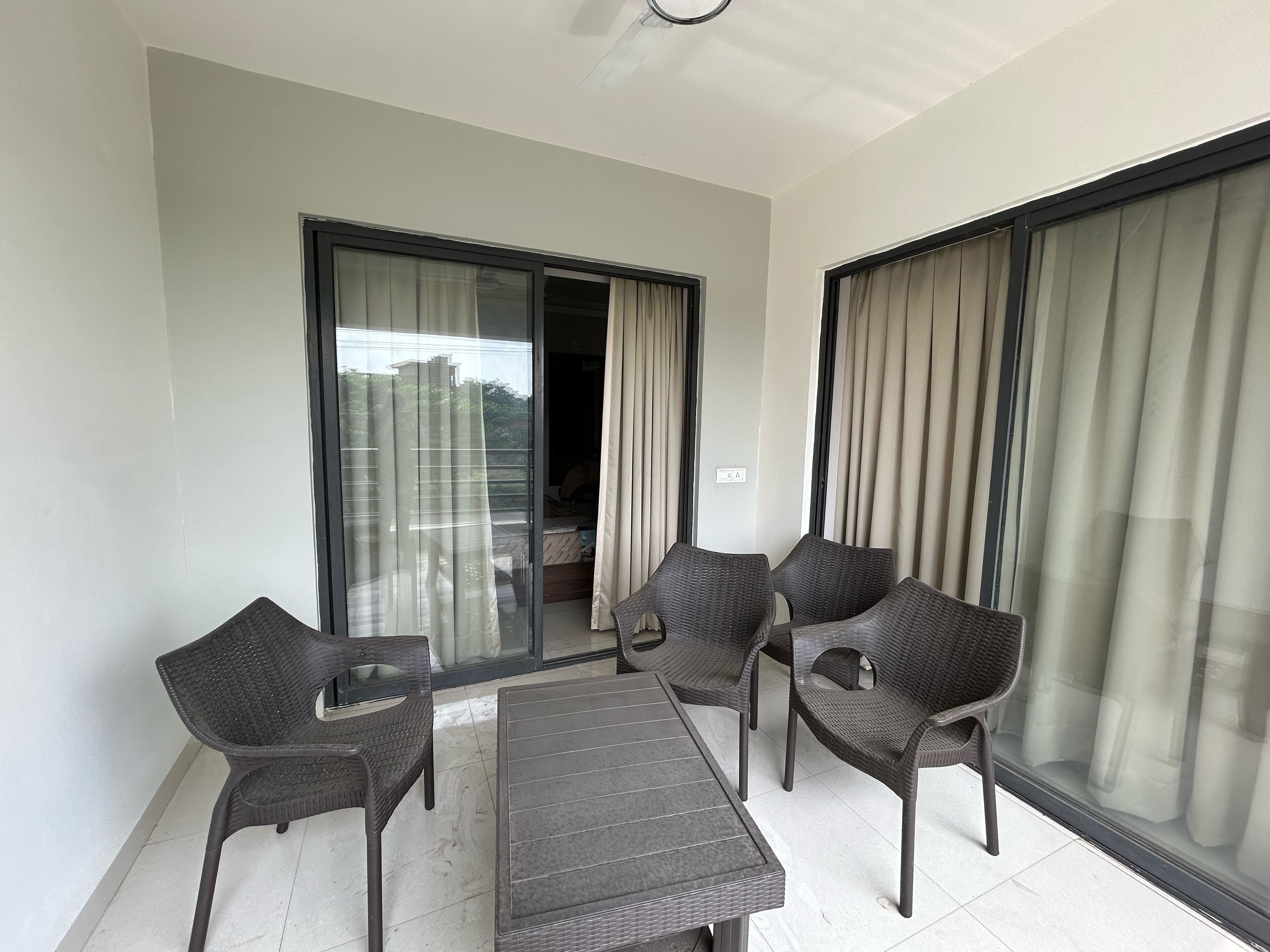 Ein Balkon mit Tisch und Stühlen, große Fenster mit Vorhängen und ein Deckenventilator.