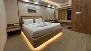 A modern hotel room with a large bed, two chairs, a small table, and a painting on the wall. - The Pearl Club Resort (Bolpur)