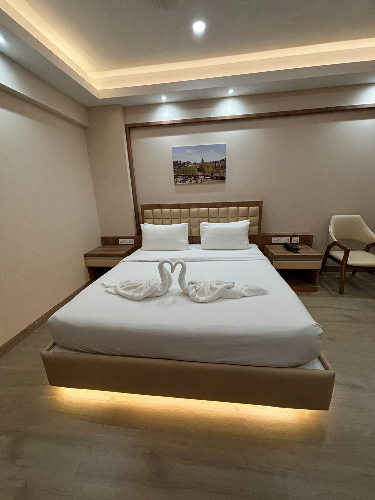 A hotel room with a large bed, two nightstands, a chair, and a framed picture on the wall.