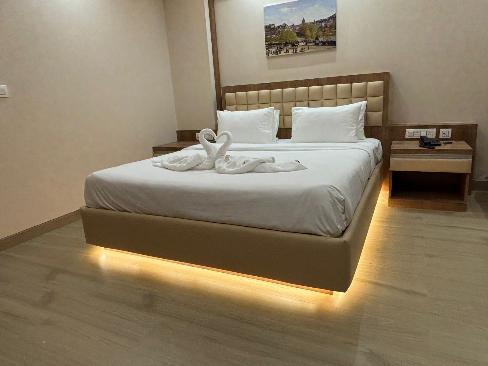Une chambre d’hôtel avec un grand lit, une tête de lit, une table de chevet et un tableau au mur.