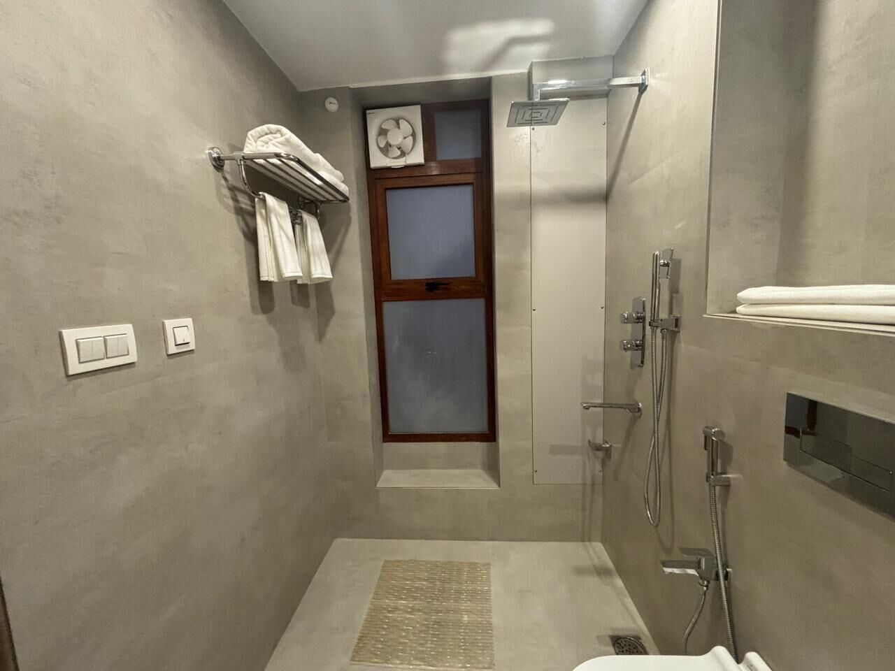 A modern bathroom with a shower, a towel rack, a fan, and a door with frosted glass panels.