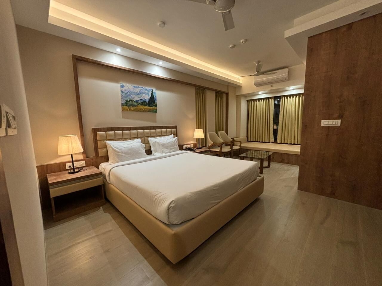 A modern hotel room with a large bed, bedside lamps, a painting on the wall, and a wooden wardrobe.