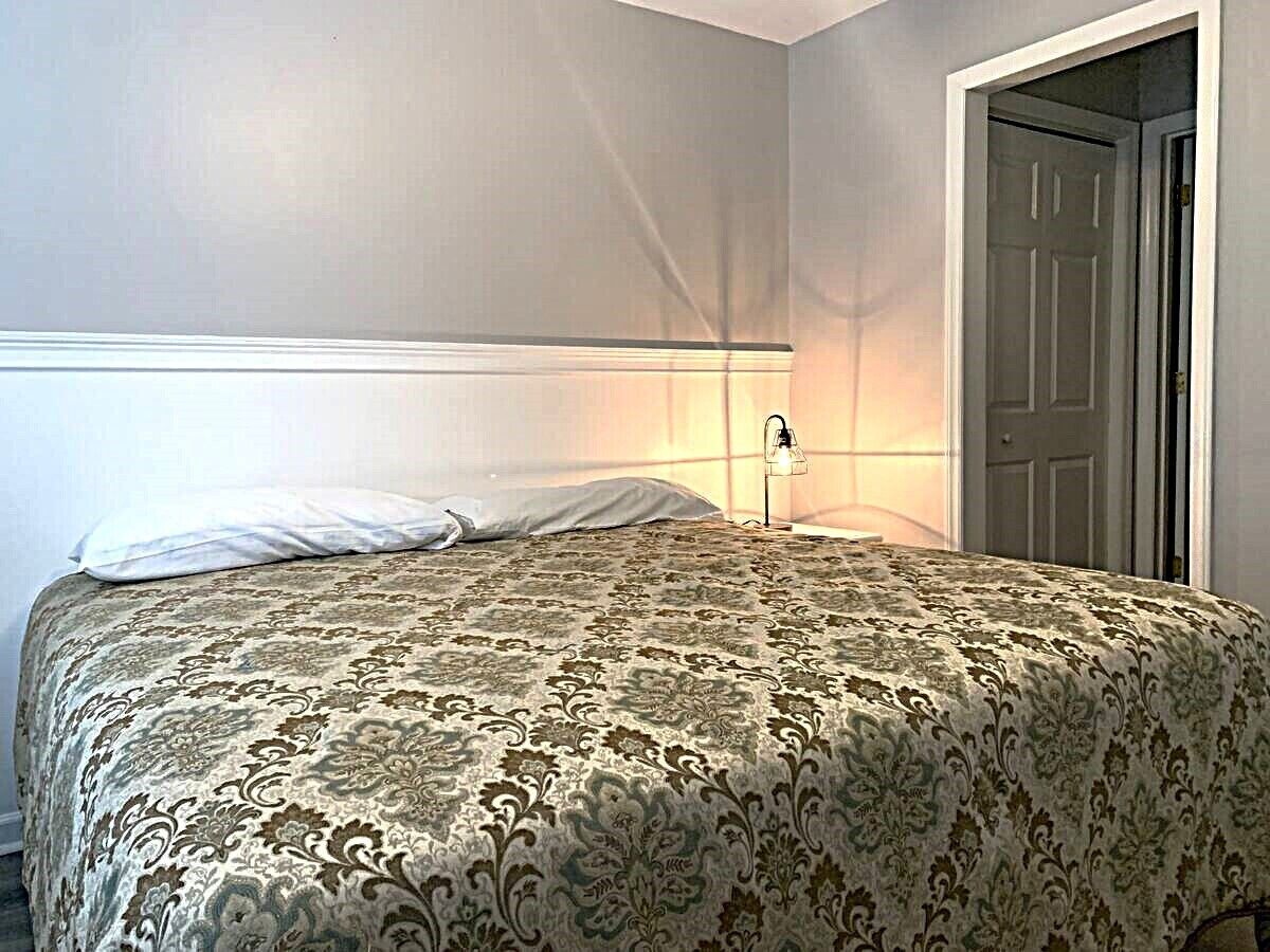 A bedroom with a bed, a nightstand, a lamp, and a door.