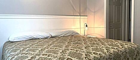 A bedroom with a bed, a nightstand, a lamp, and a door.