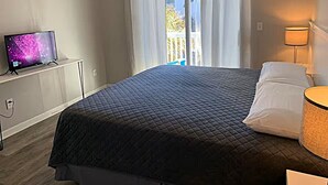 A hotel room with a bed, a TV on a stand, a lamp, and a view of the outside.