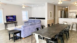 A modern living room with a sofa, a dining table with chairs, a TV, and a kitchen area.