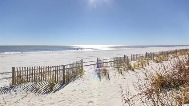 A beach with a wooden fence and sand dunes.