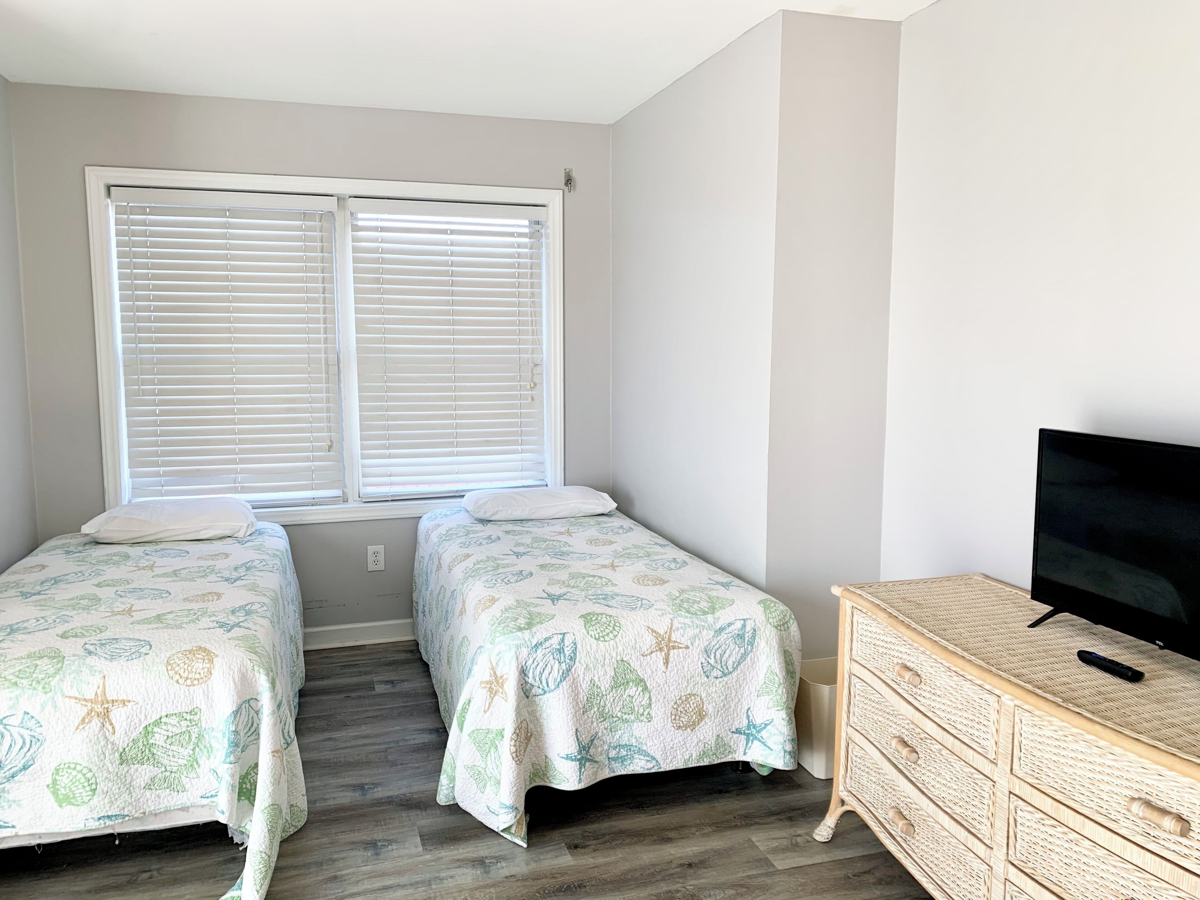A bedroom with two beds, a TV, and a wicker dresser.