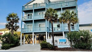 A multi-story building with balconies, palm trees, and a sign indicating it is a hotel.