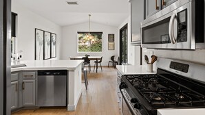 A modern kitchen with a central island, stainless steel appliances, and a dining area with a chandelier. - Eastside Costa Mesa Home Walking Distance to Back Bay Newport Beach (Costa Mesa)