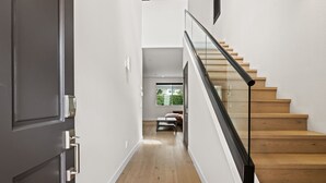 A modern interior with a wooden staircase, a dark door, and a view of a green outdoor area. - Eastside Costa Mesa Home Walking Distance to Back Bay Newport Beach (Costa Mesa)