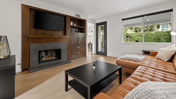 A modern living room with a fireplace, a flat-screen TV, a sofa, and a dining area visible through a glass door. - Eastside Costa Mesa Home Walking Distance to Back Bay Newport Beach (Costa Mesa)