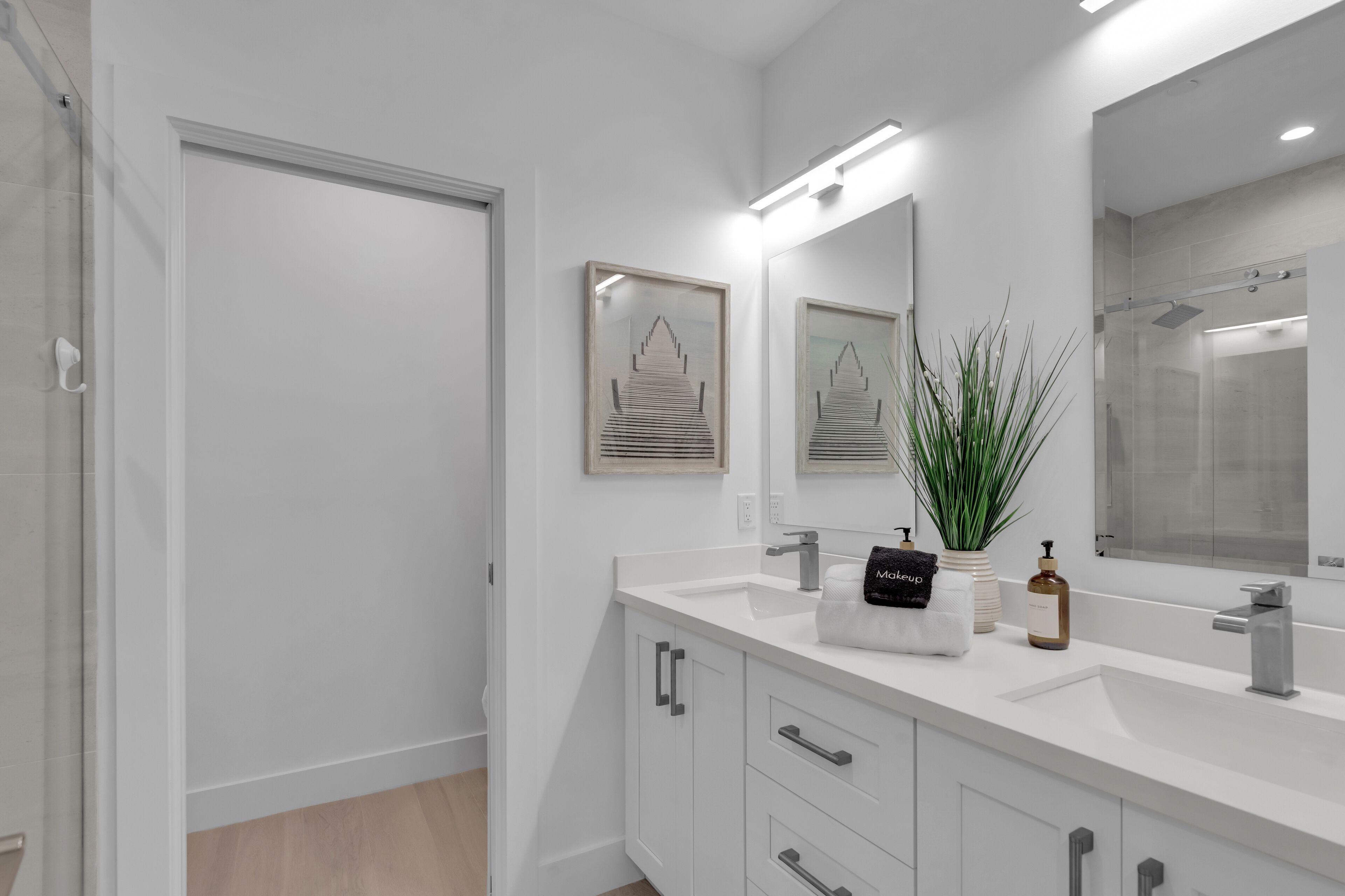 A modern bathroom with a white vanity, a large mirror, and a shower area.