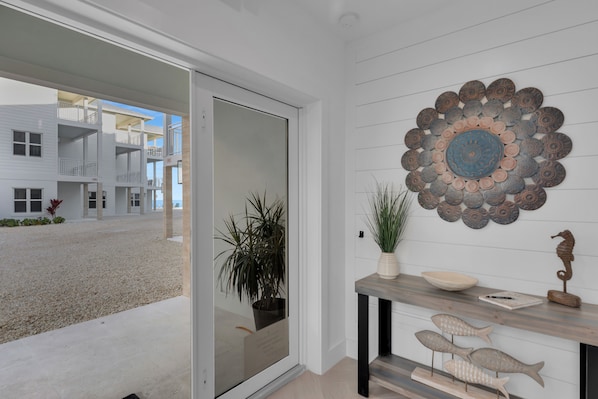 Un intérieur moderne avec une porte-fenêtre coulissante donnant sur un balcon, un élément décoratif mural et une console en bois agrémentée d’une plante et d’objets décoratifs.
