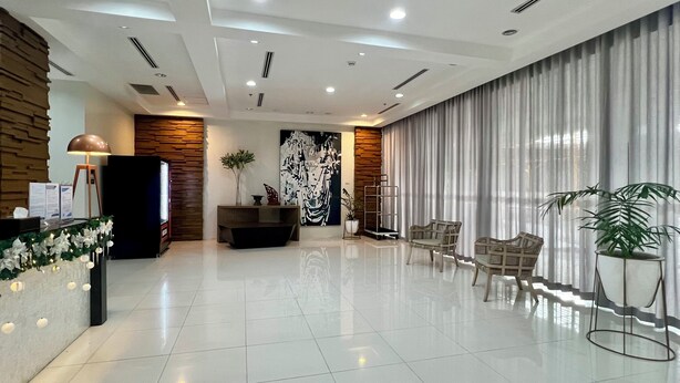 Um lobby moderno de hotel com balcão de recepção, área de estar e uma grande janela com cortinas.