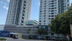 Um edifício moderno de arranha-céu, com vários andares e varandas, céu claro e uma passadeira pedonal em primeiro plano.