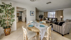 Un comedor con una mesa redonda, sillas y una planta en maceta. Hay un sofá y una lámpara en la sala de estar.