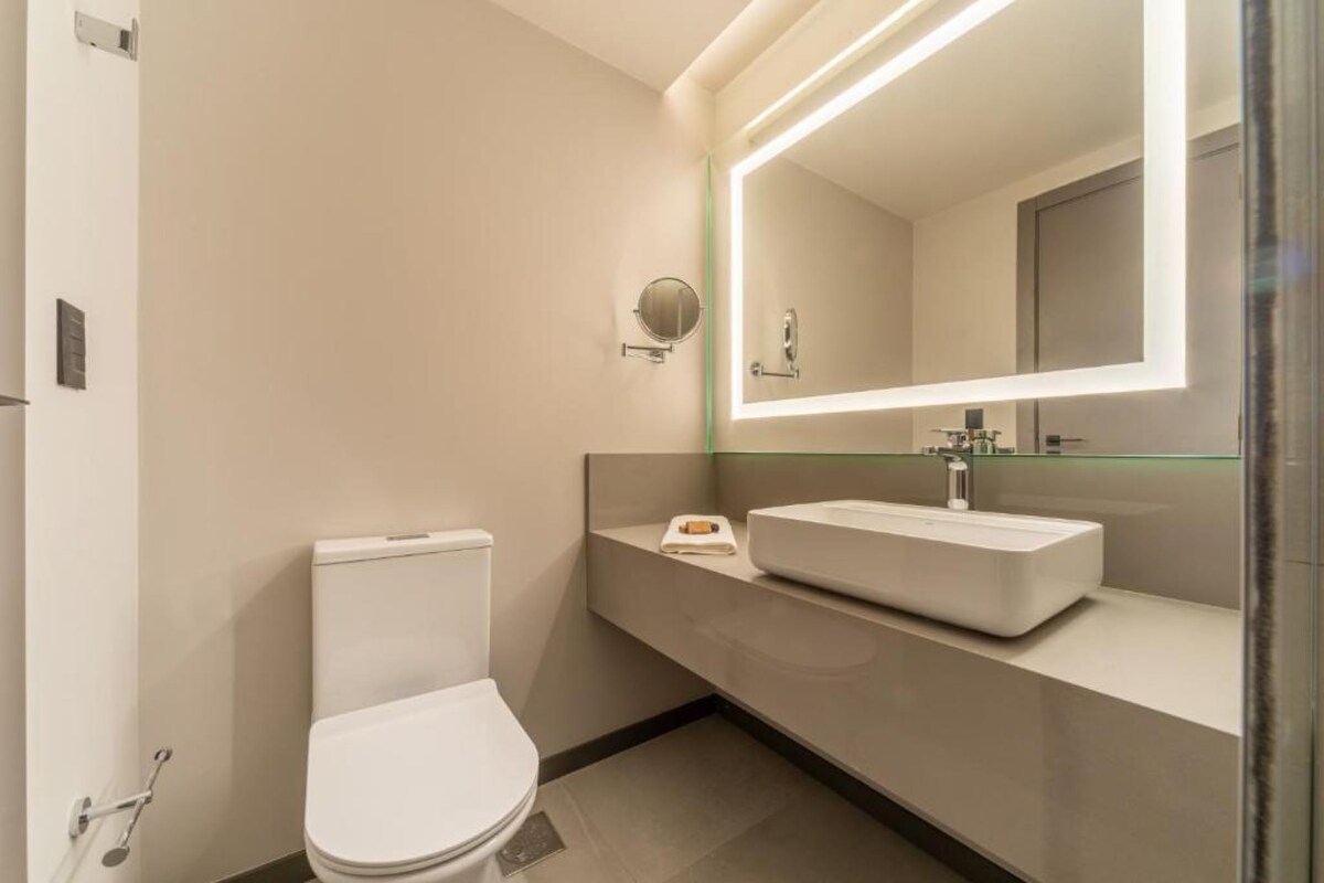 A modern bathroom with a toilet, a sink, and a large mirror.
