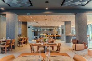 A modern dining area with wooden tables and chairs, a bar area in the background, and a ceiling with geometric patterns. - Laghetto Stilo Garden (Gramado)