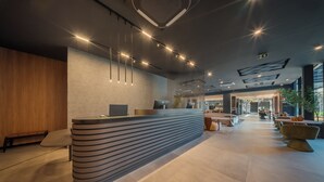 A modern reception area with a curved reception desk, seating area, and a view of the lobby. - Laghetto Stilo Garden (Gramado)