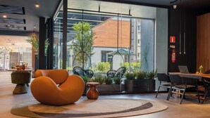 A modern interior with a large window, a round orange chair, a wooden table, and a laptop on a desk. - Laghetto Stilo Garden (Gramado)