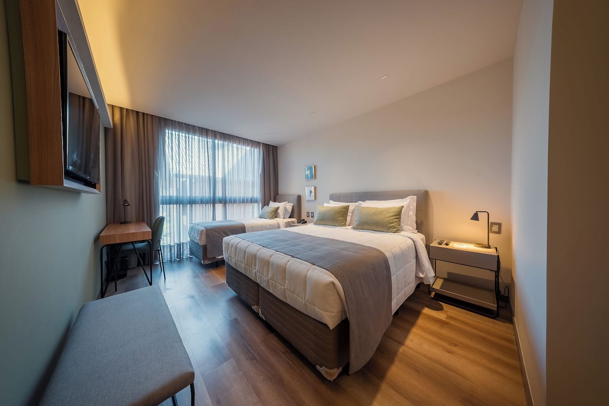 A modern hotel room with a large bed, a desk, and a bench.