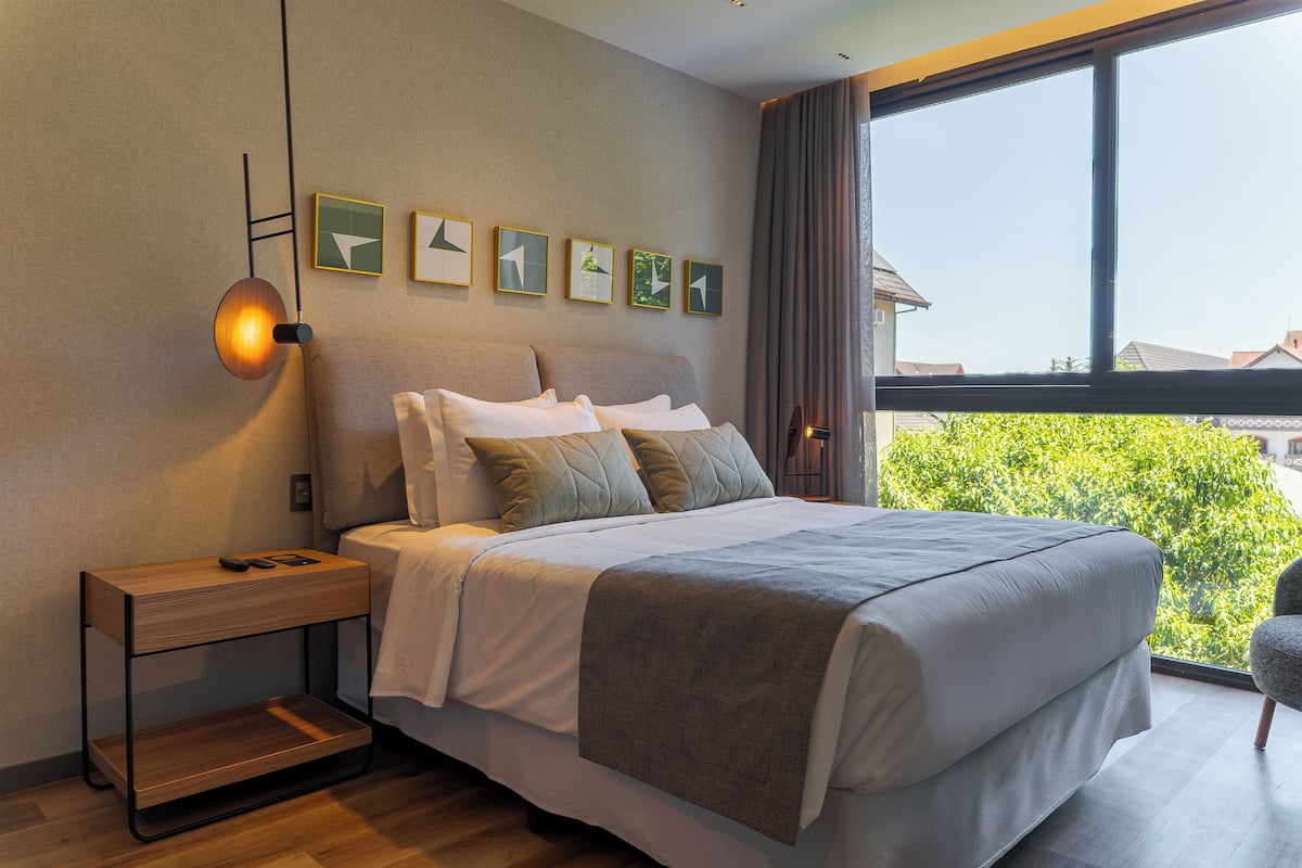 A modern bedroom with a large bed, bedside tables, and a view of greenery outside.