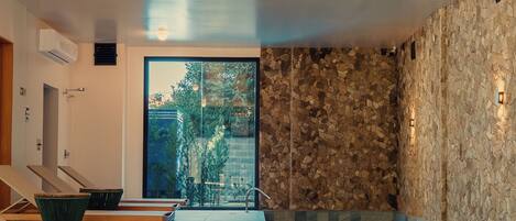 A modern indoor pool area with a stone wall, a view of greenery outside, and lounge chairs.