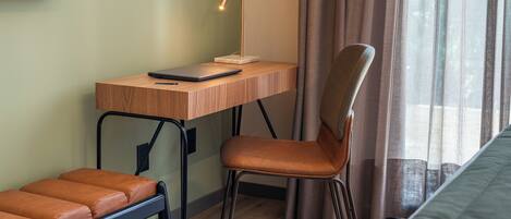 A room with a wooden desk, a chair, a laptop, a smartphone, and a bench.