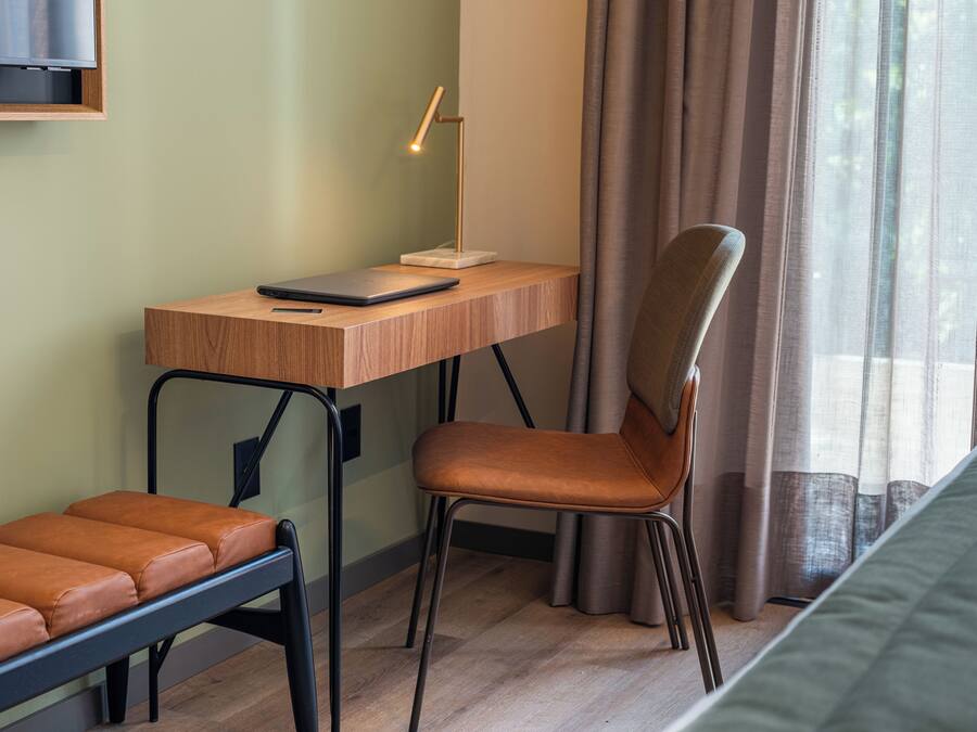 A room with a wooden desk, a chair, a laptop, a smartphone, and a bench.