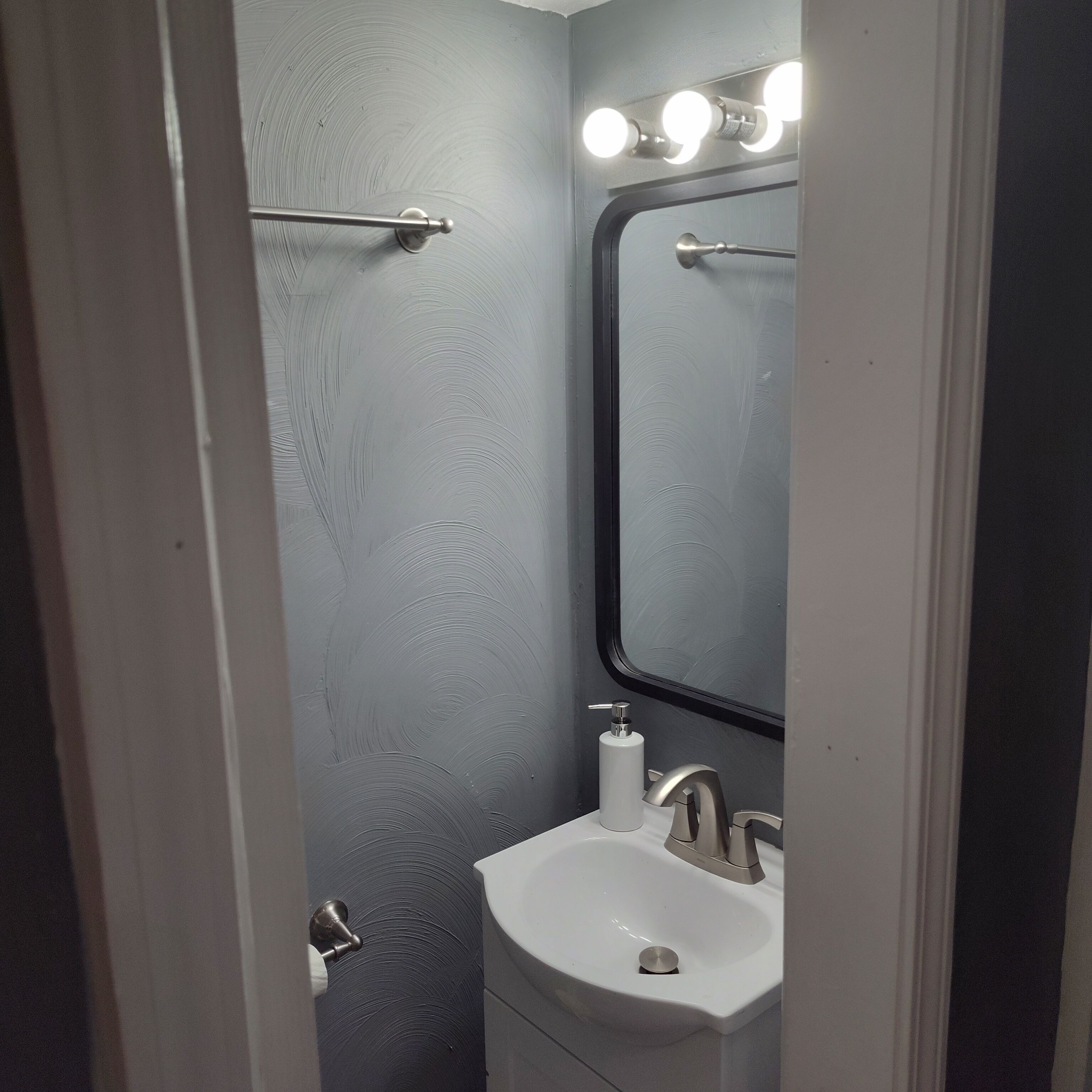 Un baño con lavamanos blanco, un espejo y un perchero para toallas.